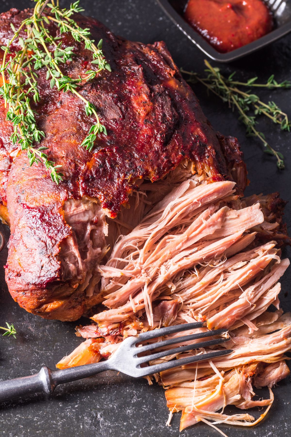 A fork shredding a roasted pork loin.