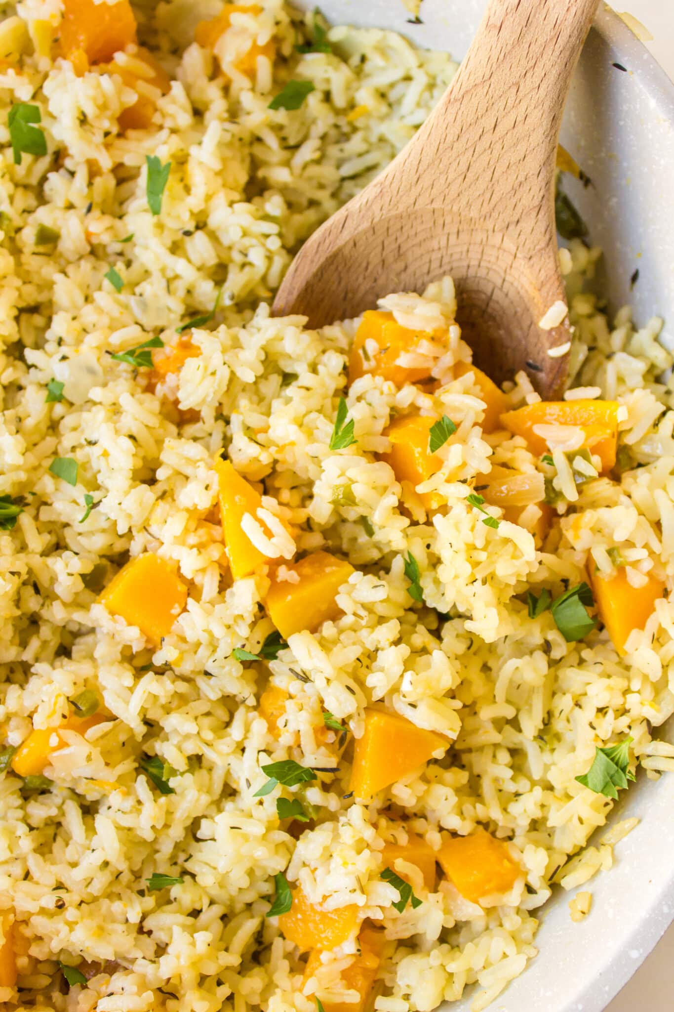 A wooden spoon in a pot of pumpkin rice.