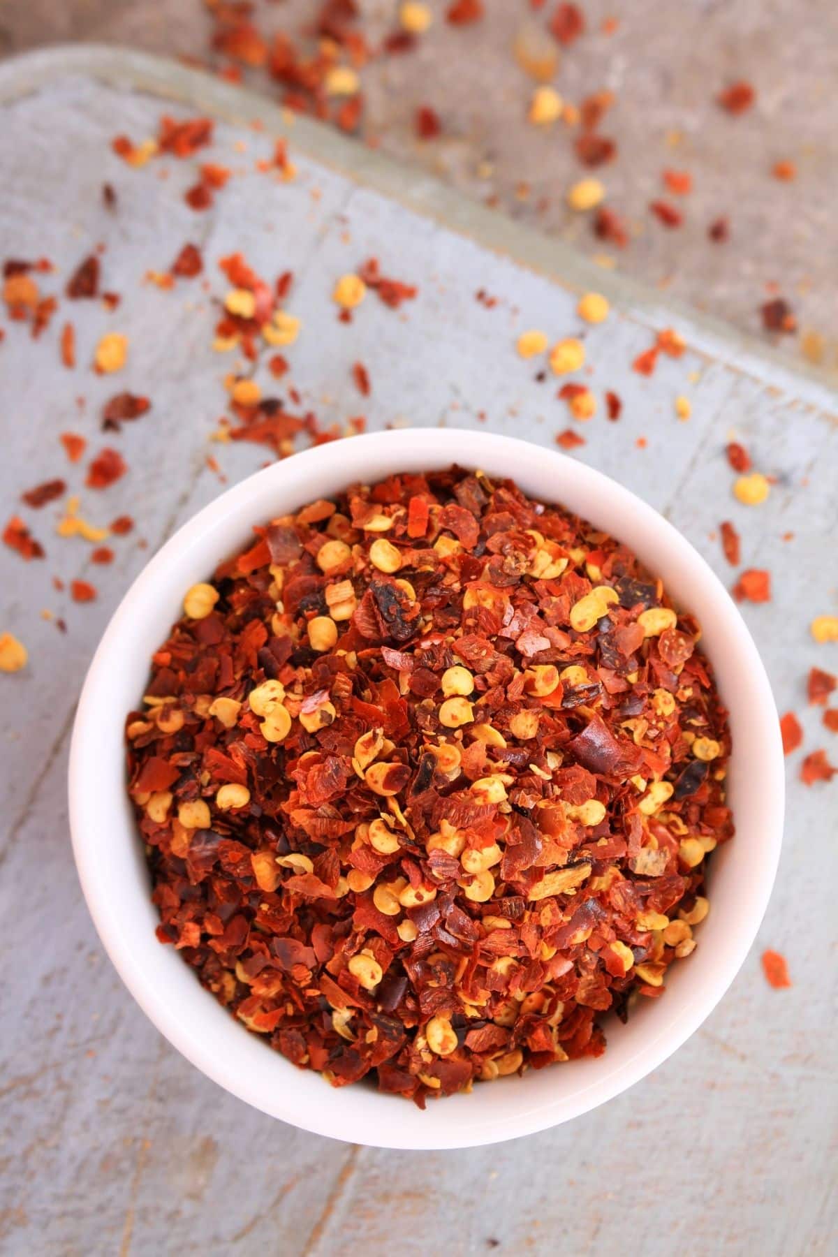 Bowl of red pepper flakes on wooden surface.