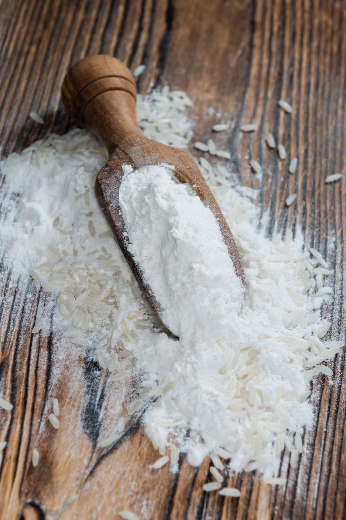 Scoop of rice flour with grains of rice on wooden surface.