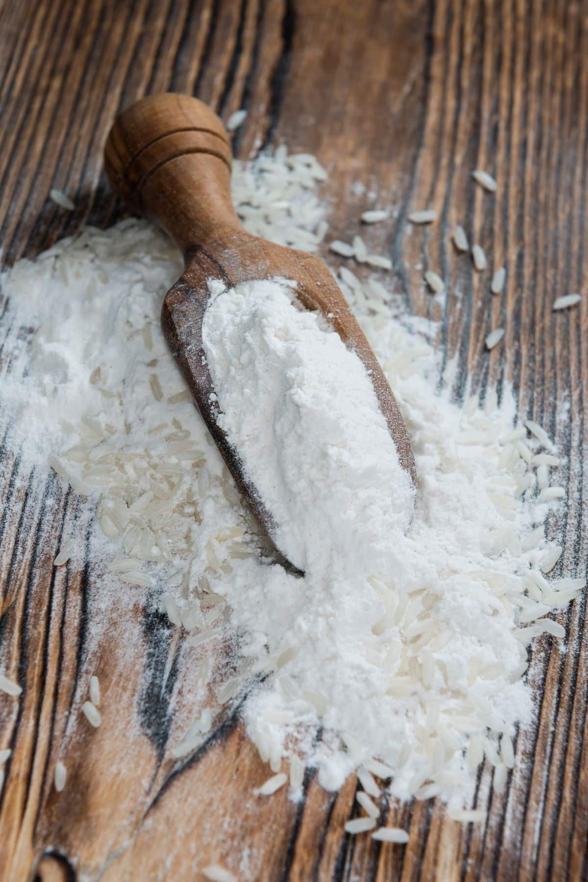 Scoop of rice flour with grains of rice on wooden surface.