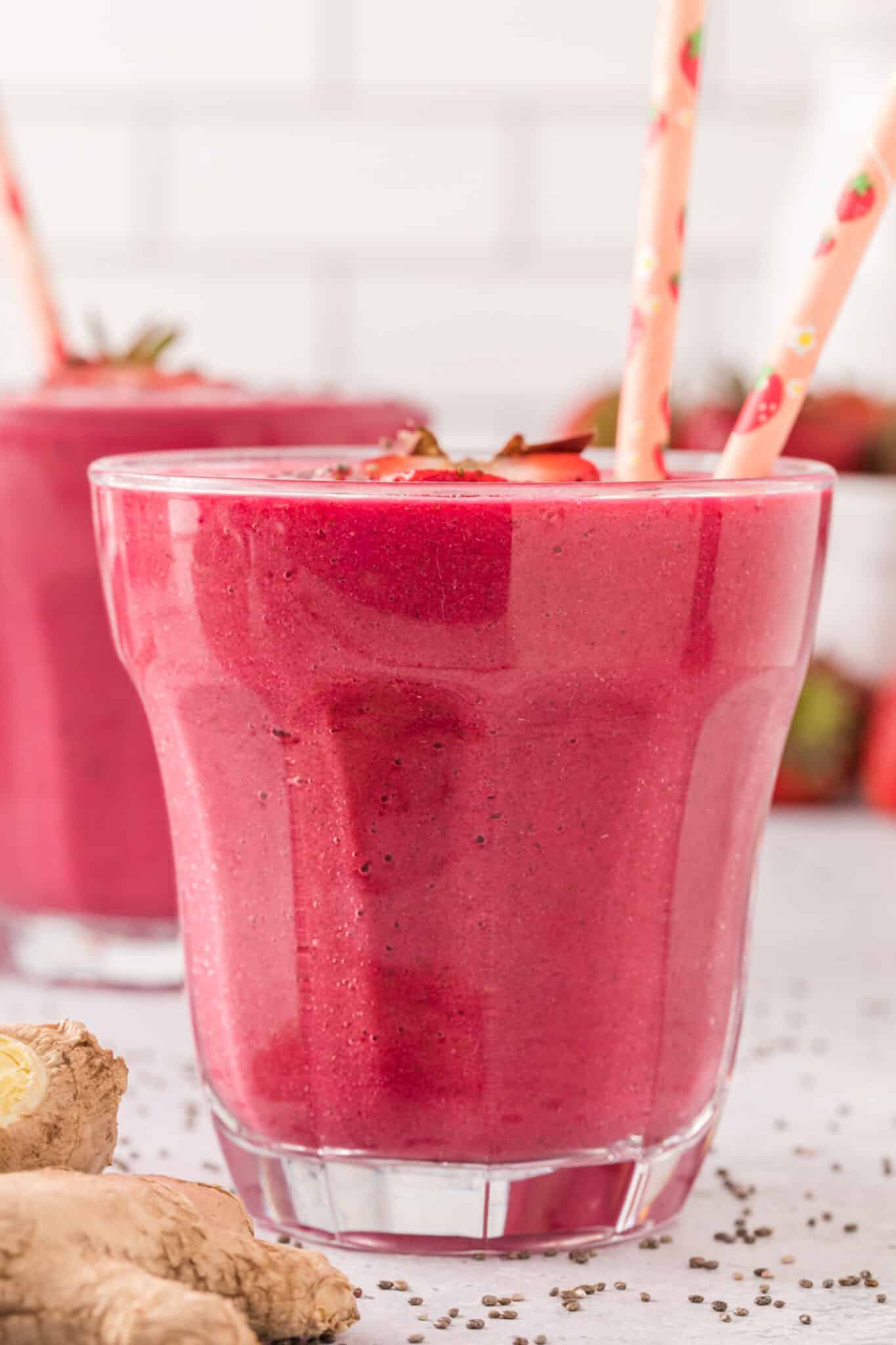 Two pink straws in a glass of strawberry smoothie topped with strawberries and chia.