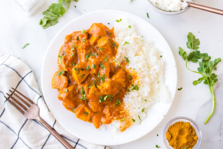 A white dinner plate loaded with white rice and chicken curry.