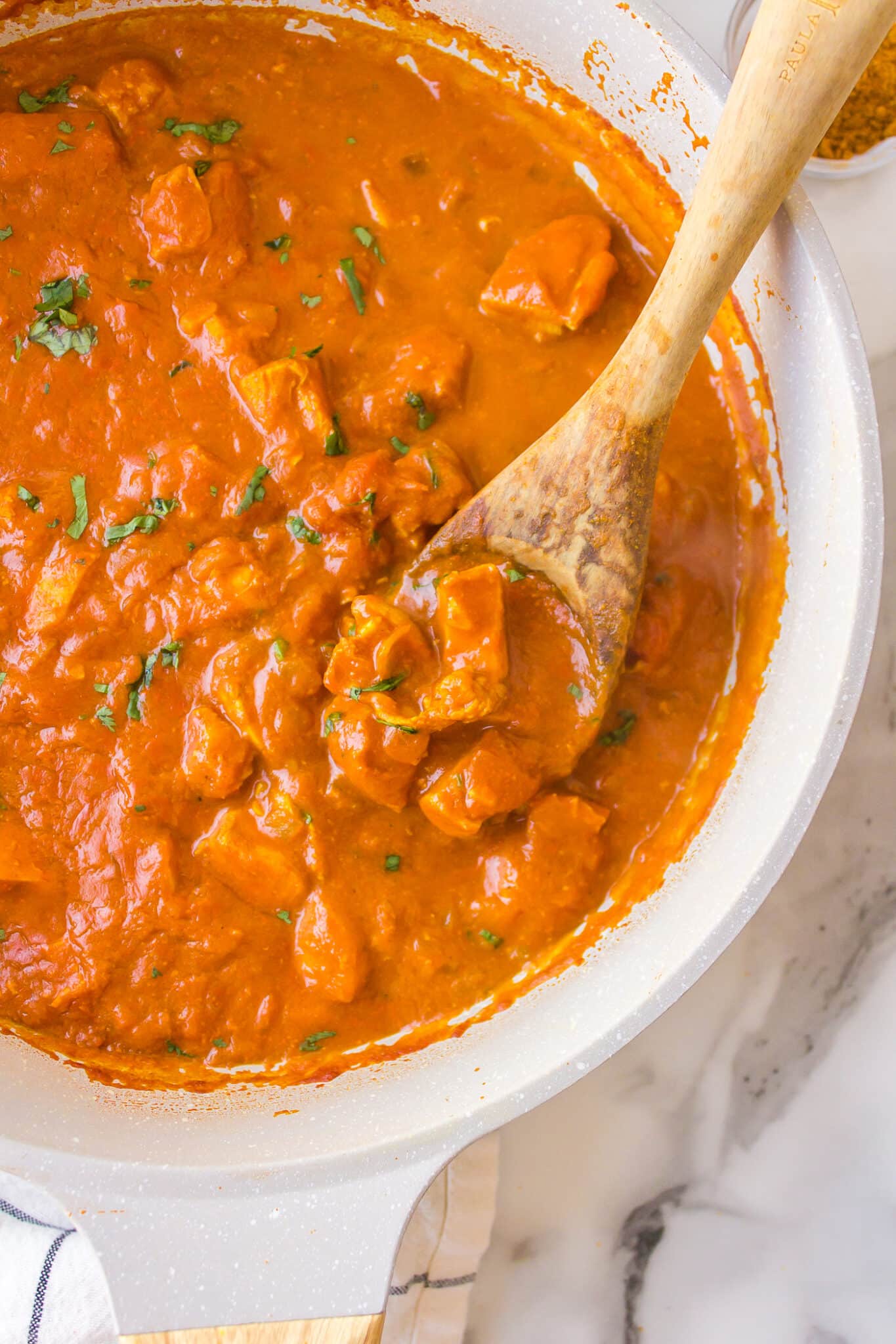 A wooden spoon in a saucepan of simple chicken curry.