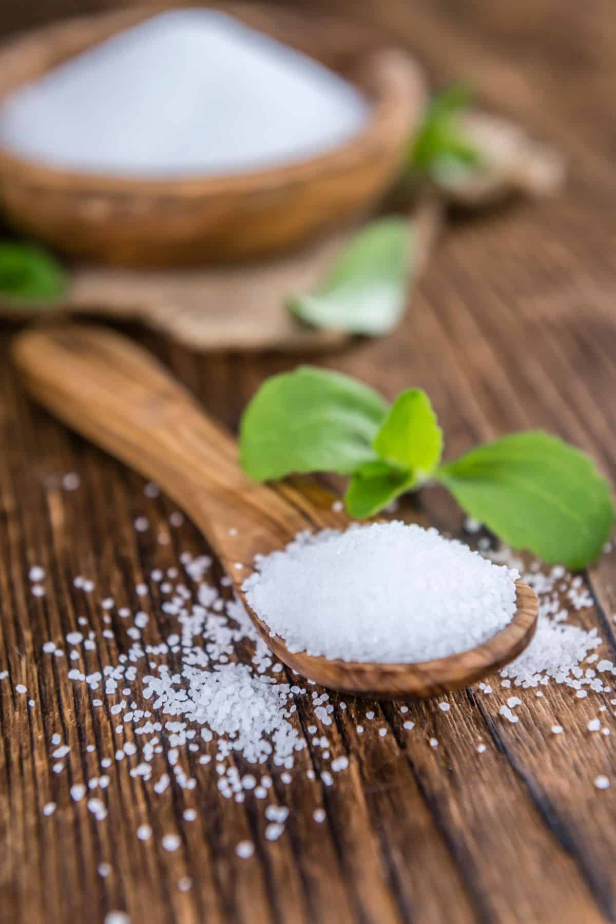 Spoonful of stevia with erythritol and fresh stevia leaves on wooden surface.