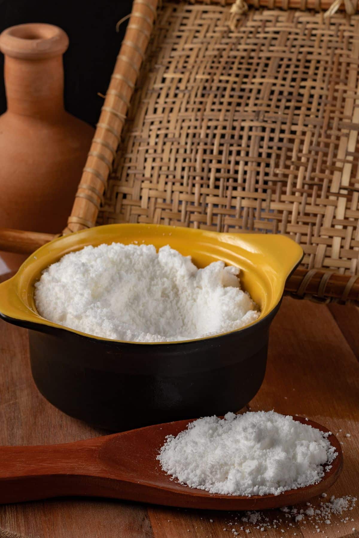 Bowl and spoonful of tapioca flour on wooden surface.