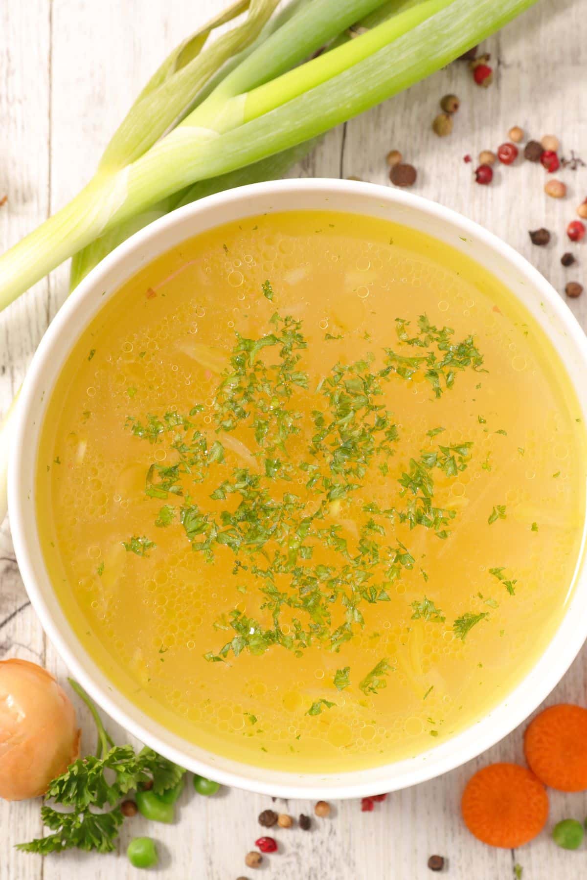 Bowl of vegetable bouillon on wooden surface.