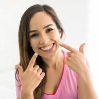 Brunette woman smiling and pointing to teeth with both index fingers.