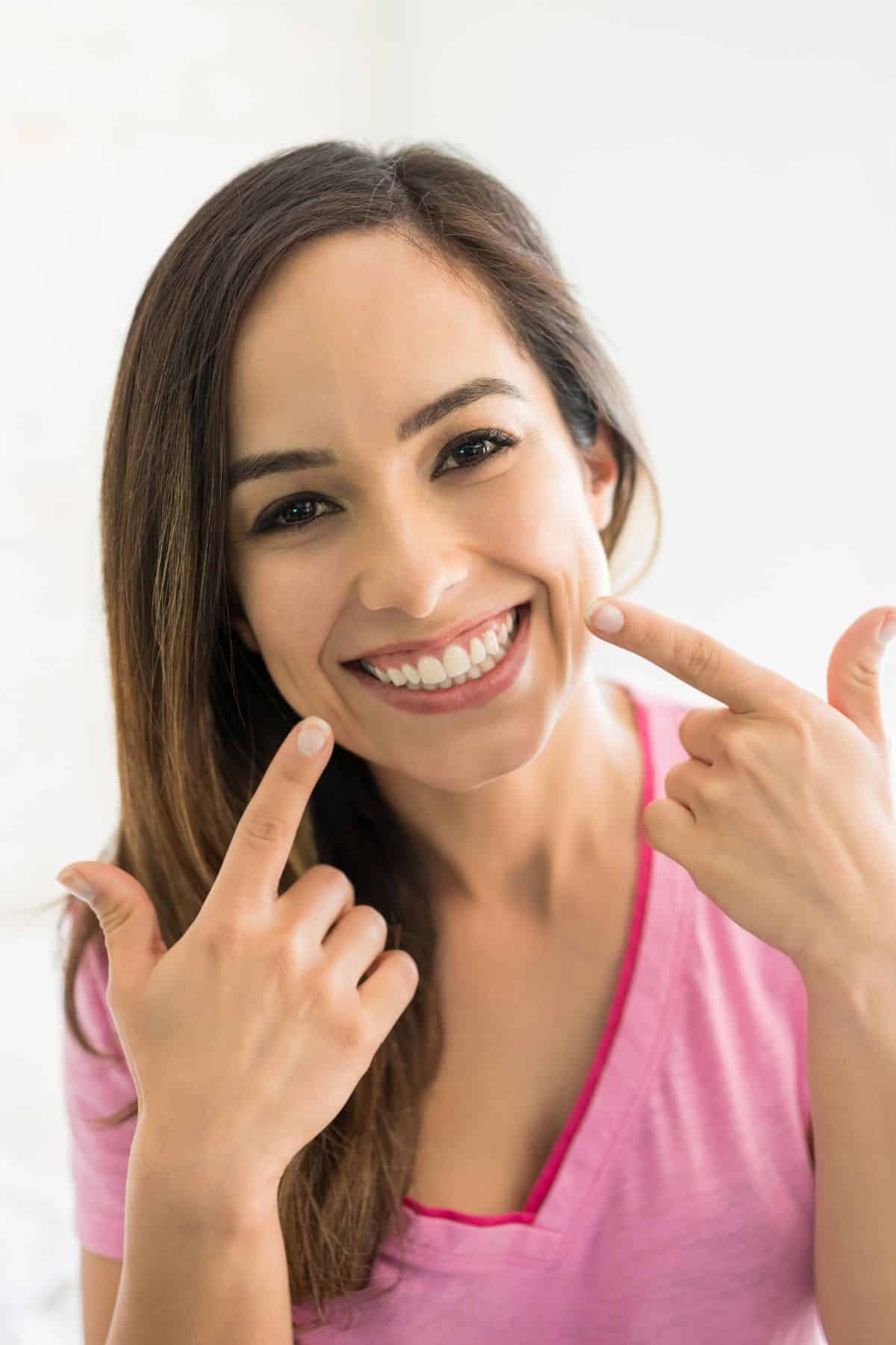 Brunette woman smiling and pointing to teeth with both index fingers.