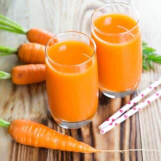 two glasses of carrot juice on a table.