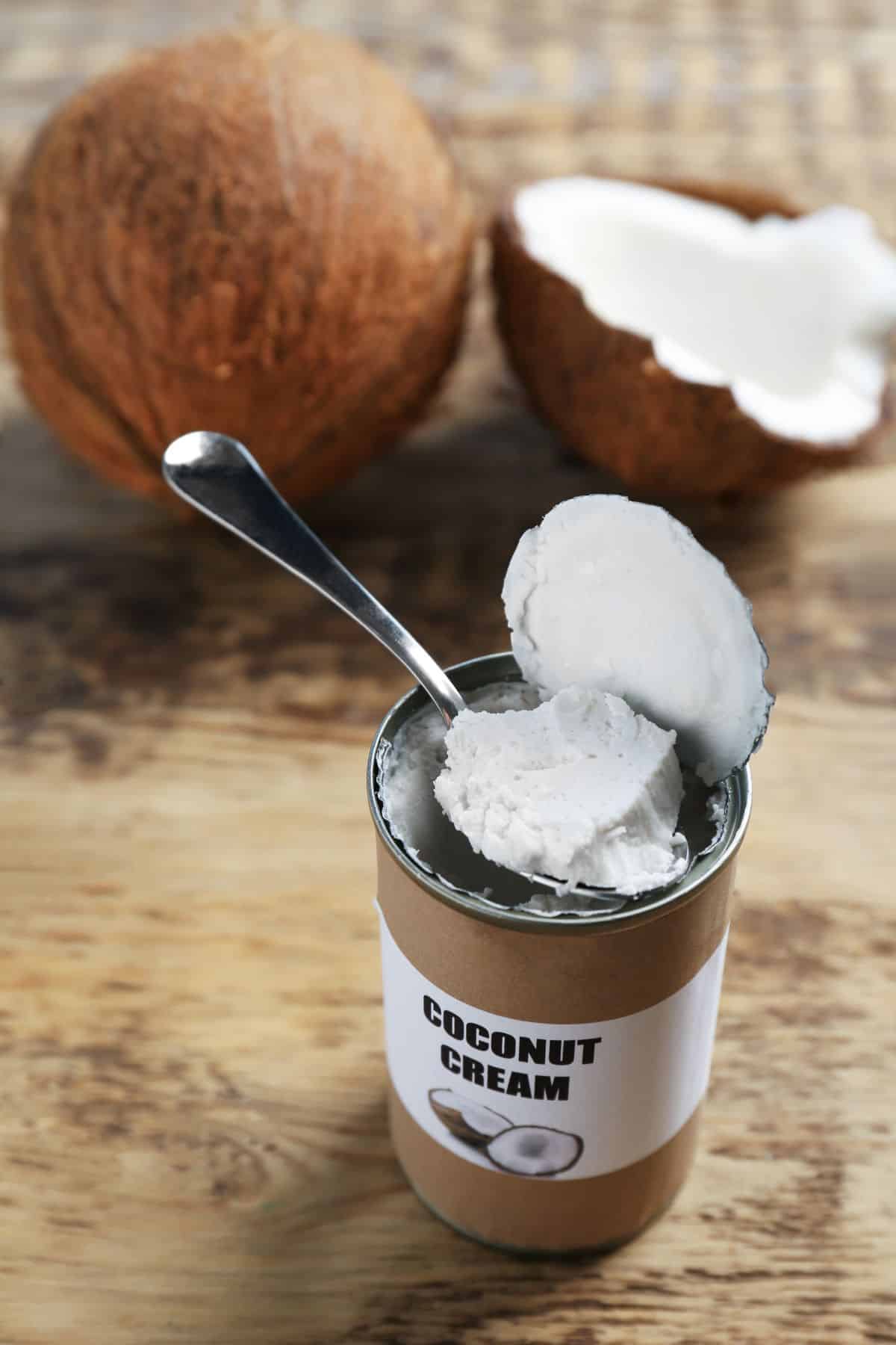 a can of opened coconut cream next to a sliced coconut.