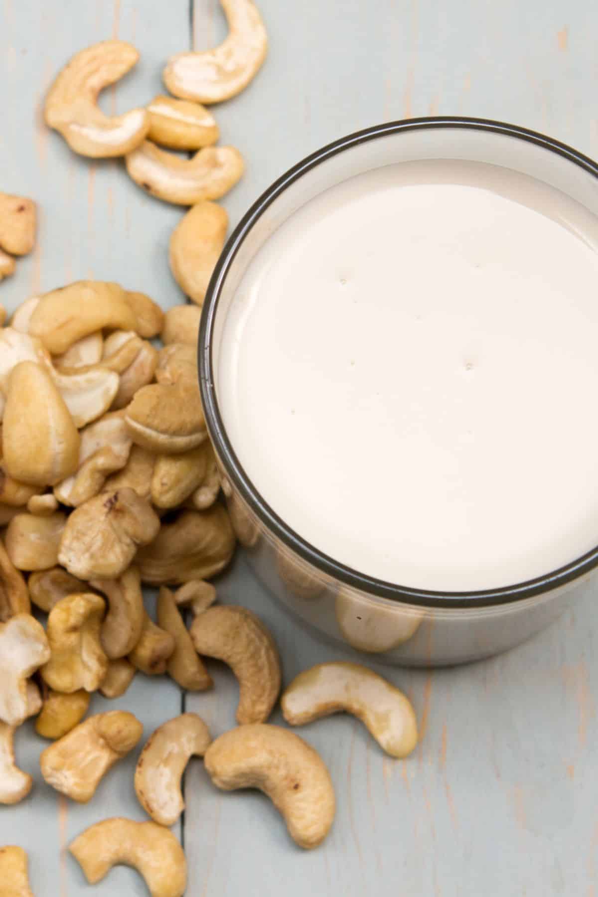 a glass of cashew cream surrounded by cashews on a table.