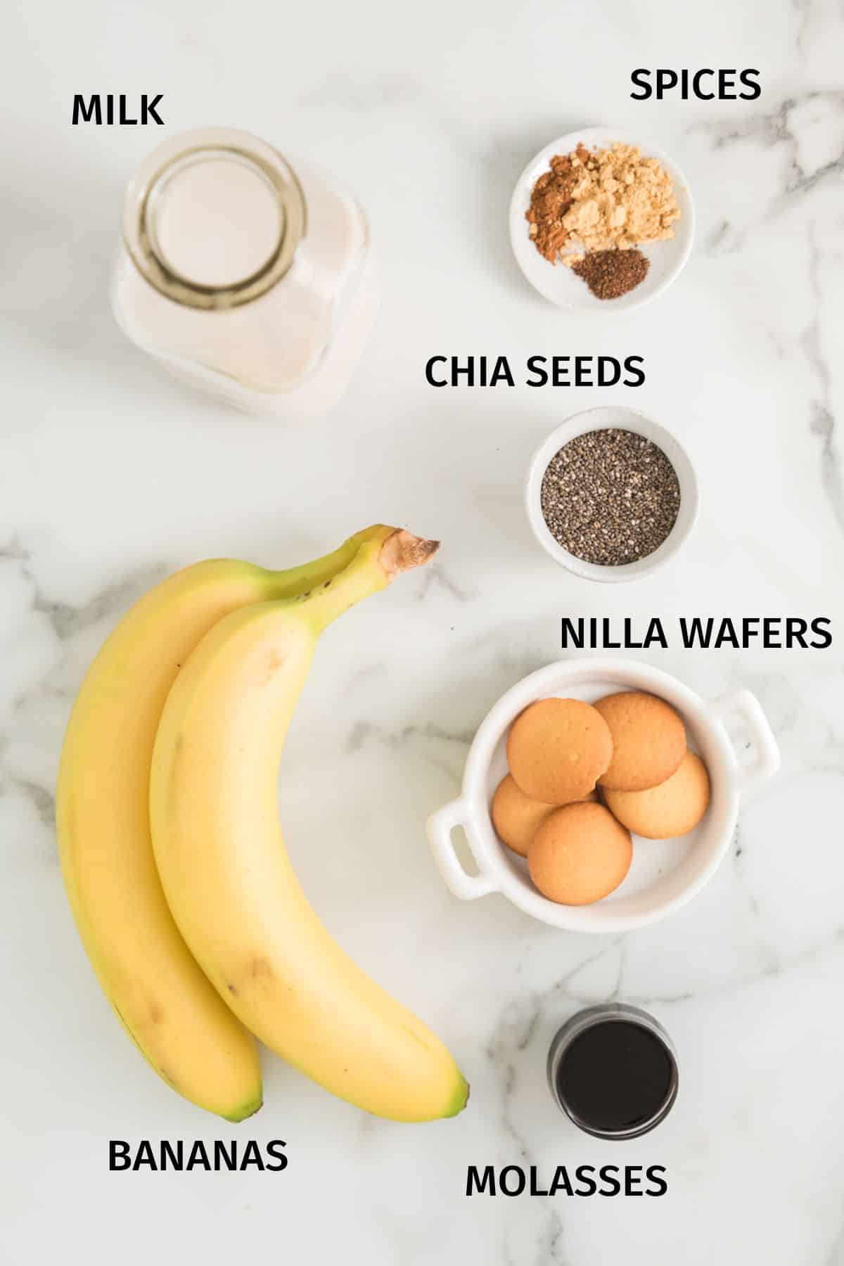 Ingredients to make a gingerbread smoothie in small bowls on a white surface.