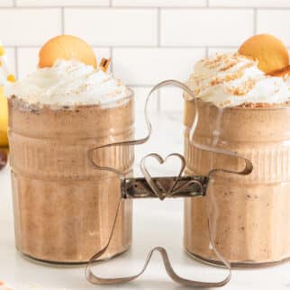 Two glasses of gingerbread smoothie topped with whipped cream and cookies.