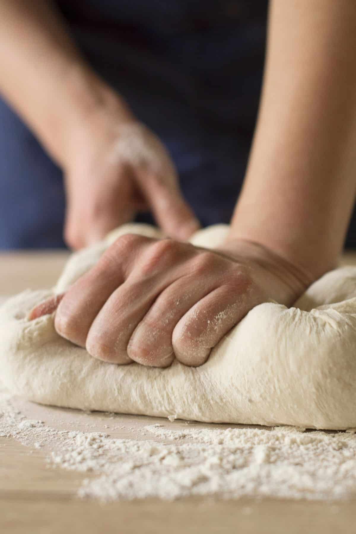 Someone kneading a ball of dough on a floured surface.