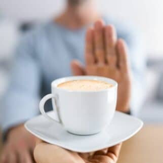 a person holding her hand out to a cup of coffee.