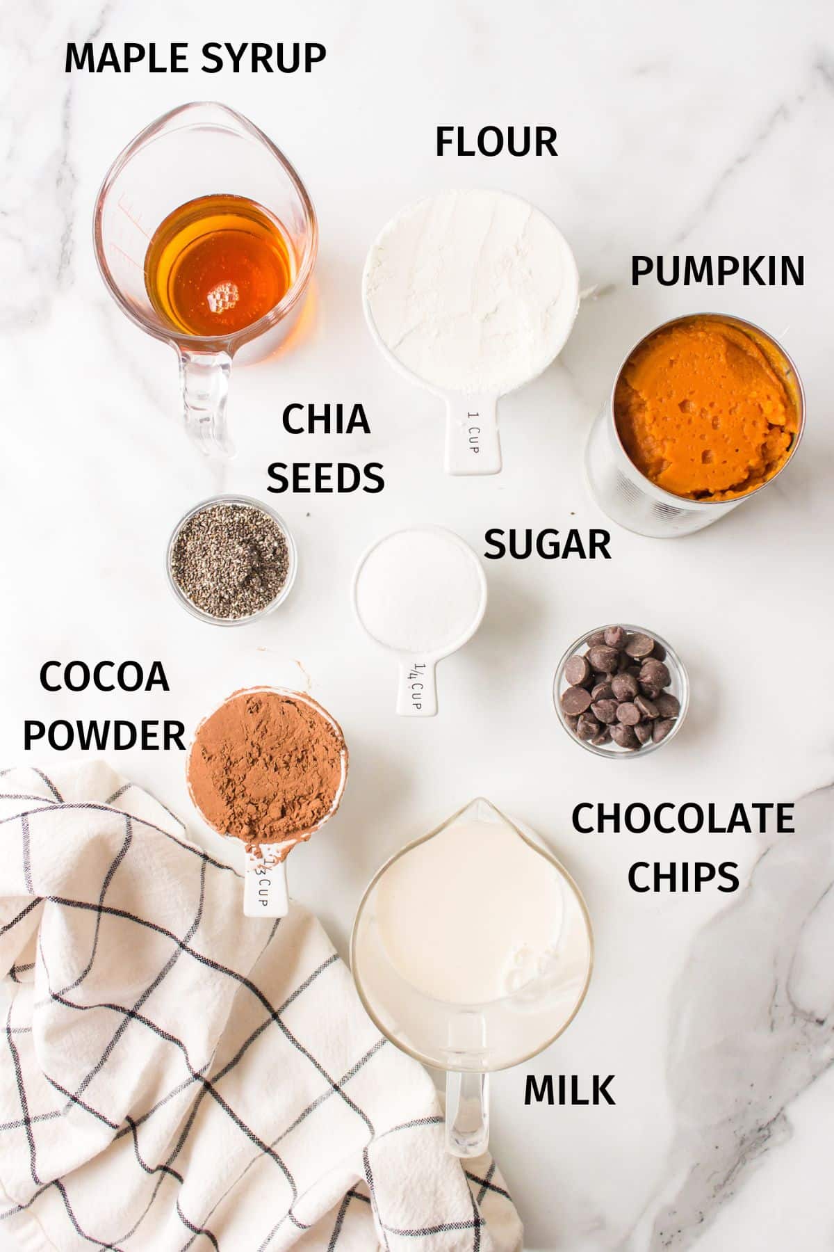 Ingredients for pumpkin brownies in small bowls on a white surface.