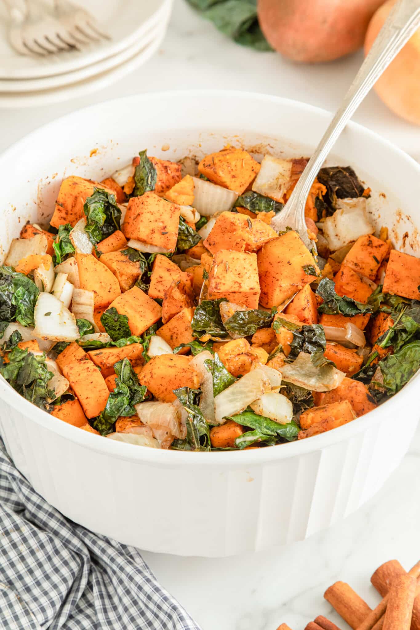 Large white ceramic bowl filled with baked kale and sweet potatoes, plus onion.
