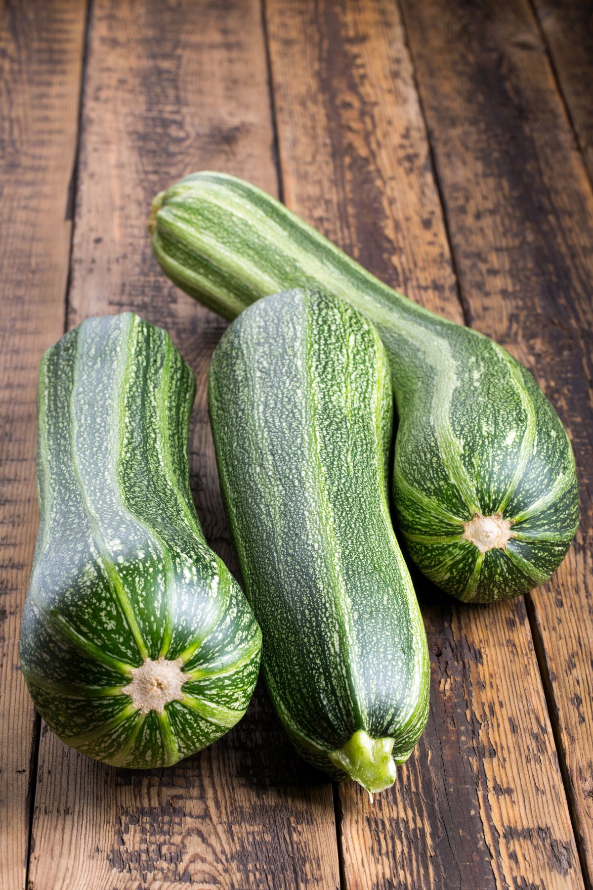 Three fresh zucchini squash on a wooden table.