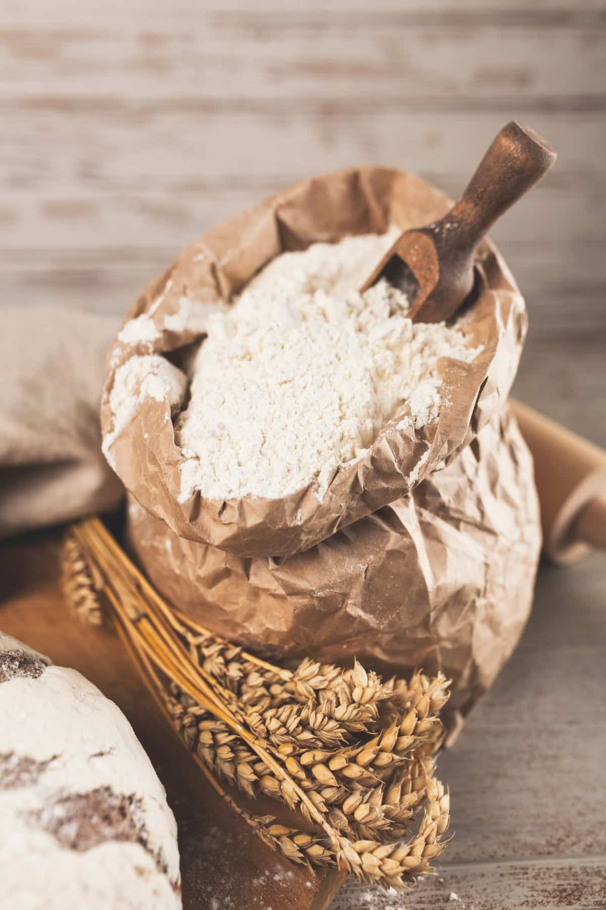 Bag of all-purpose flour with wheat on wooden surface.