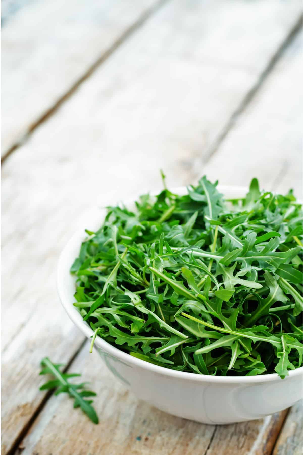 Bowl of arugula on wooden surface.