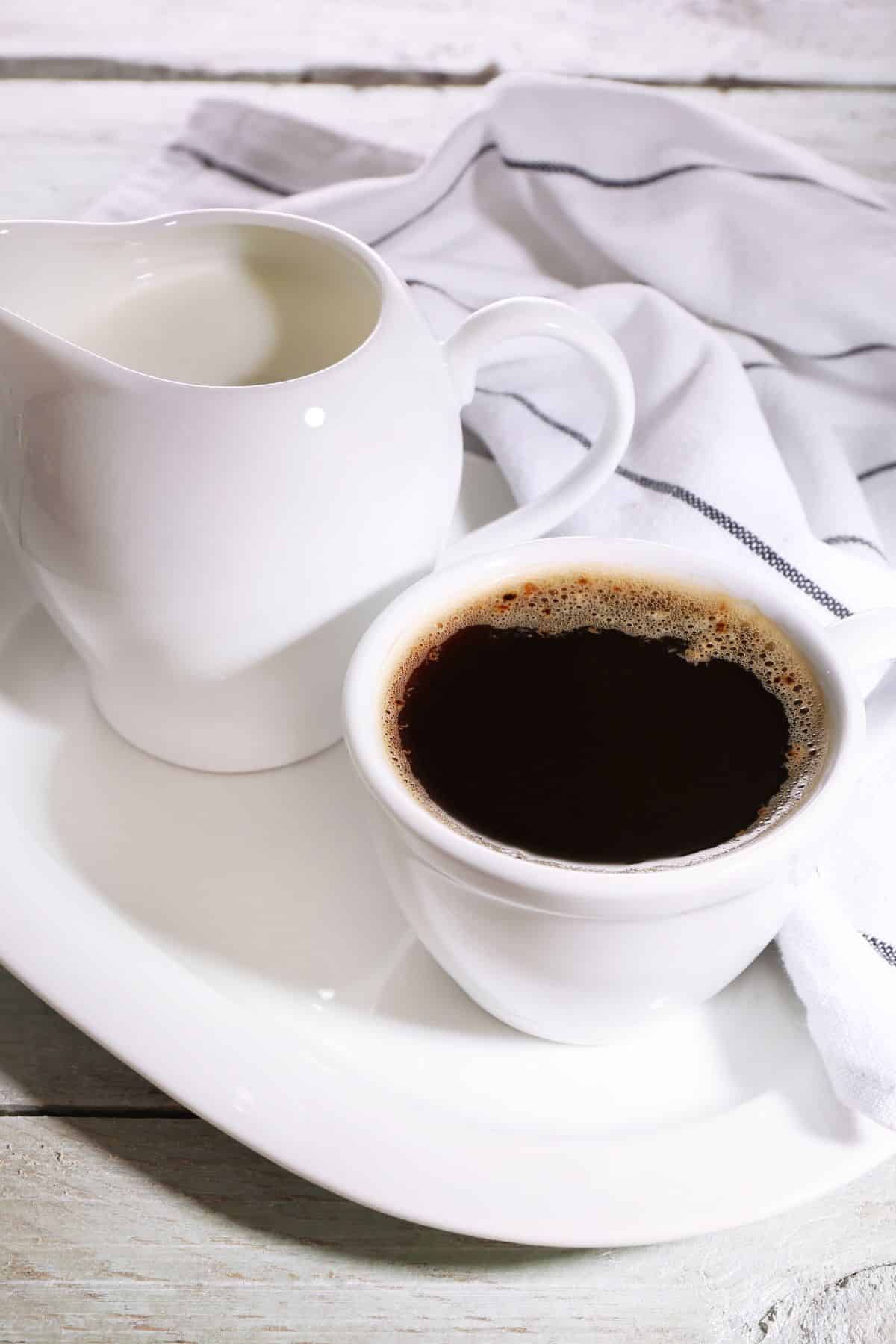 a mug of coffee beside a small pitcher of creamer.