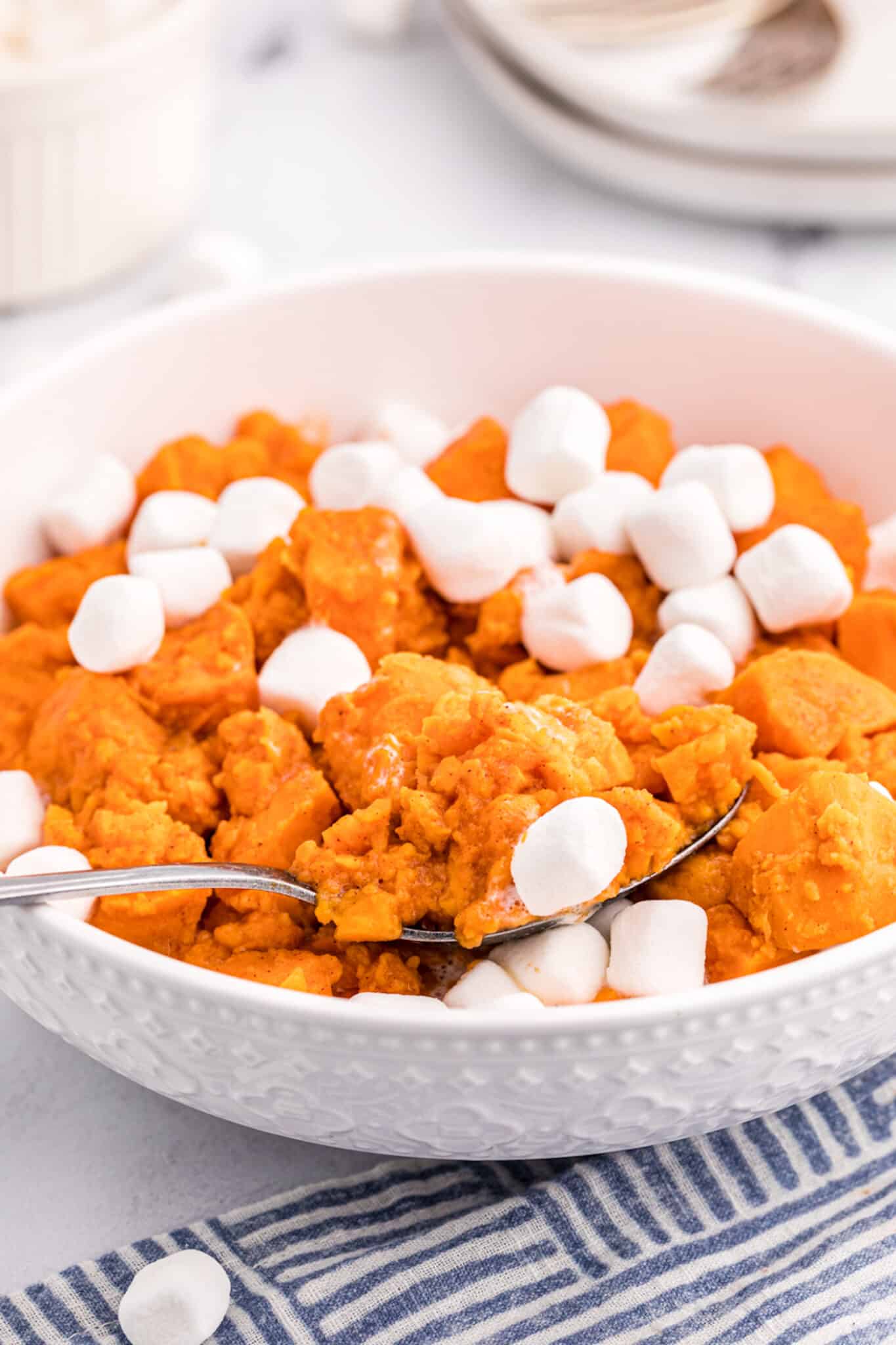 A white serving bowl with candied yams topped with marshmallows.