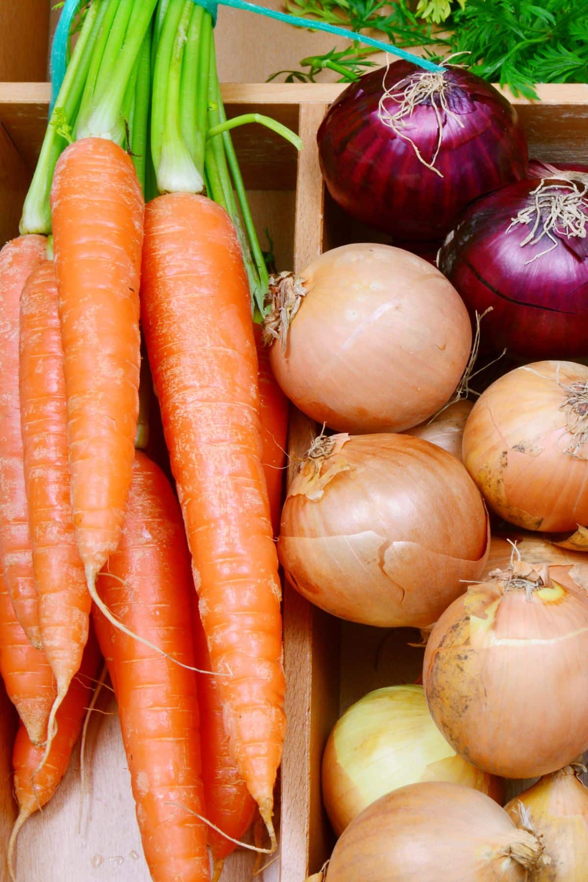 Whole carrots and onions in a wooden container.