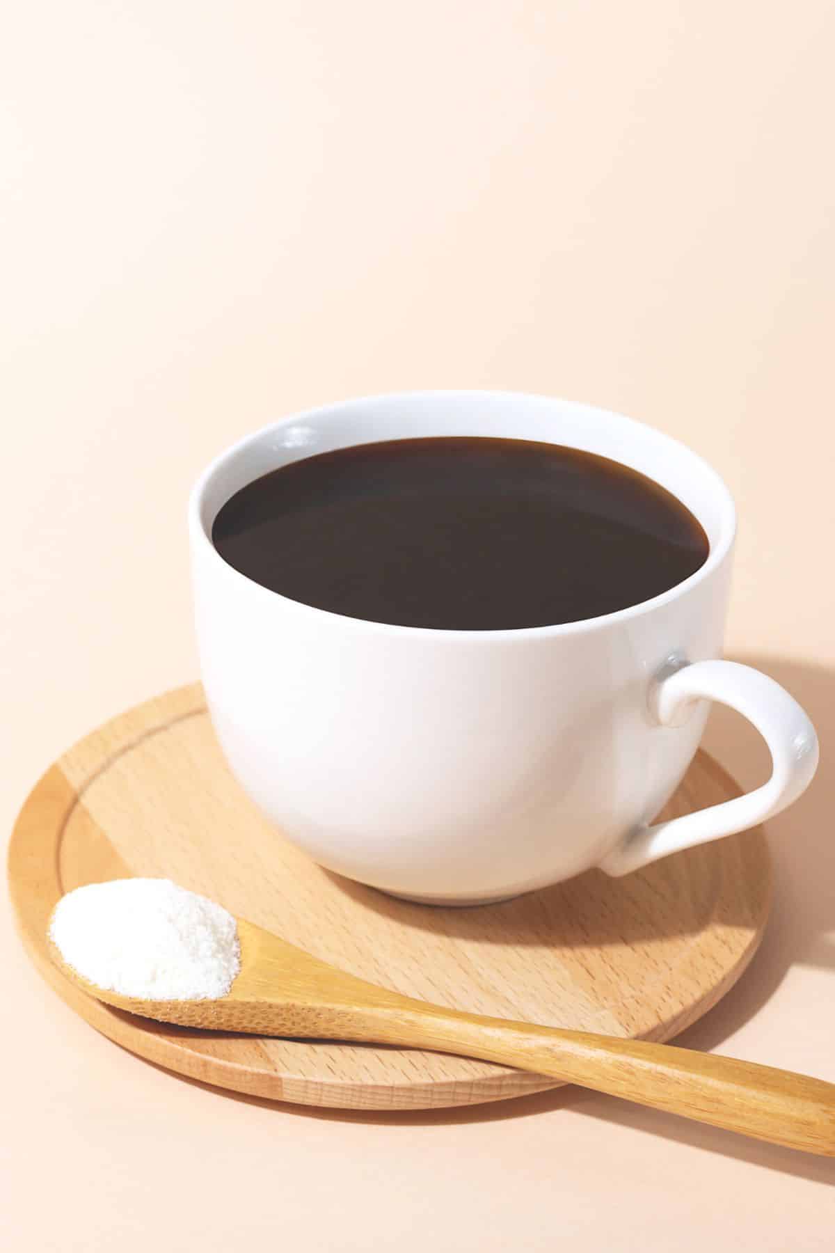 A spoon of collagen next to a white mug full of coffee.