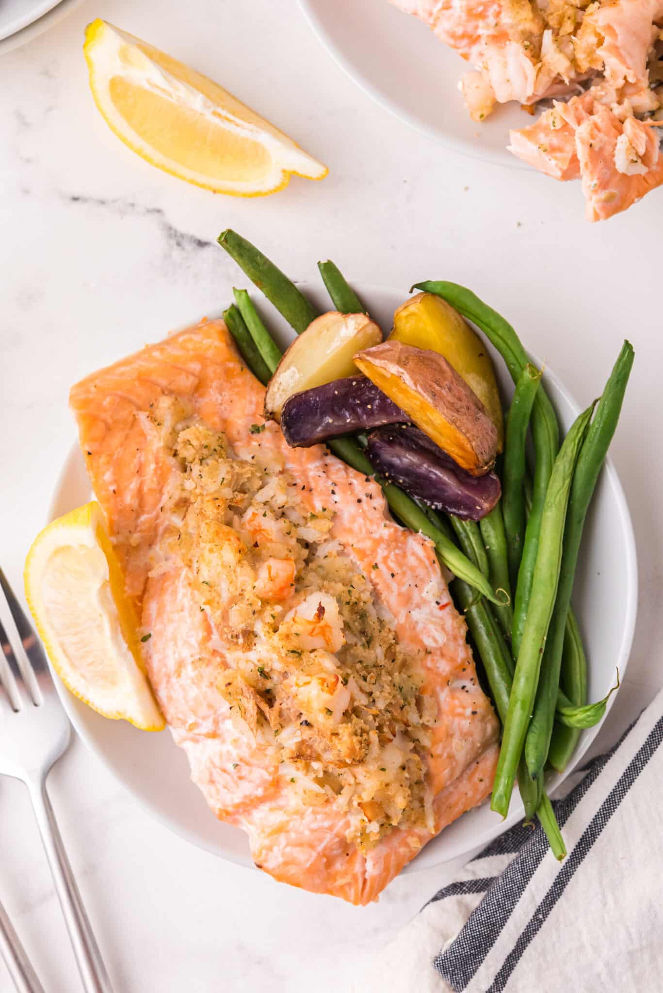A stuffed salmon filet on a white plate with green beans and potatoes.