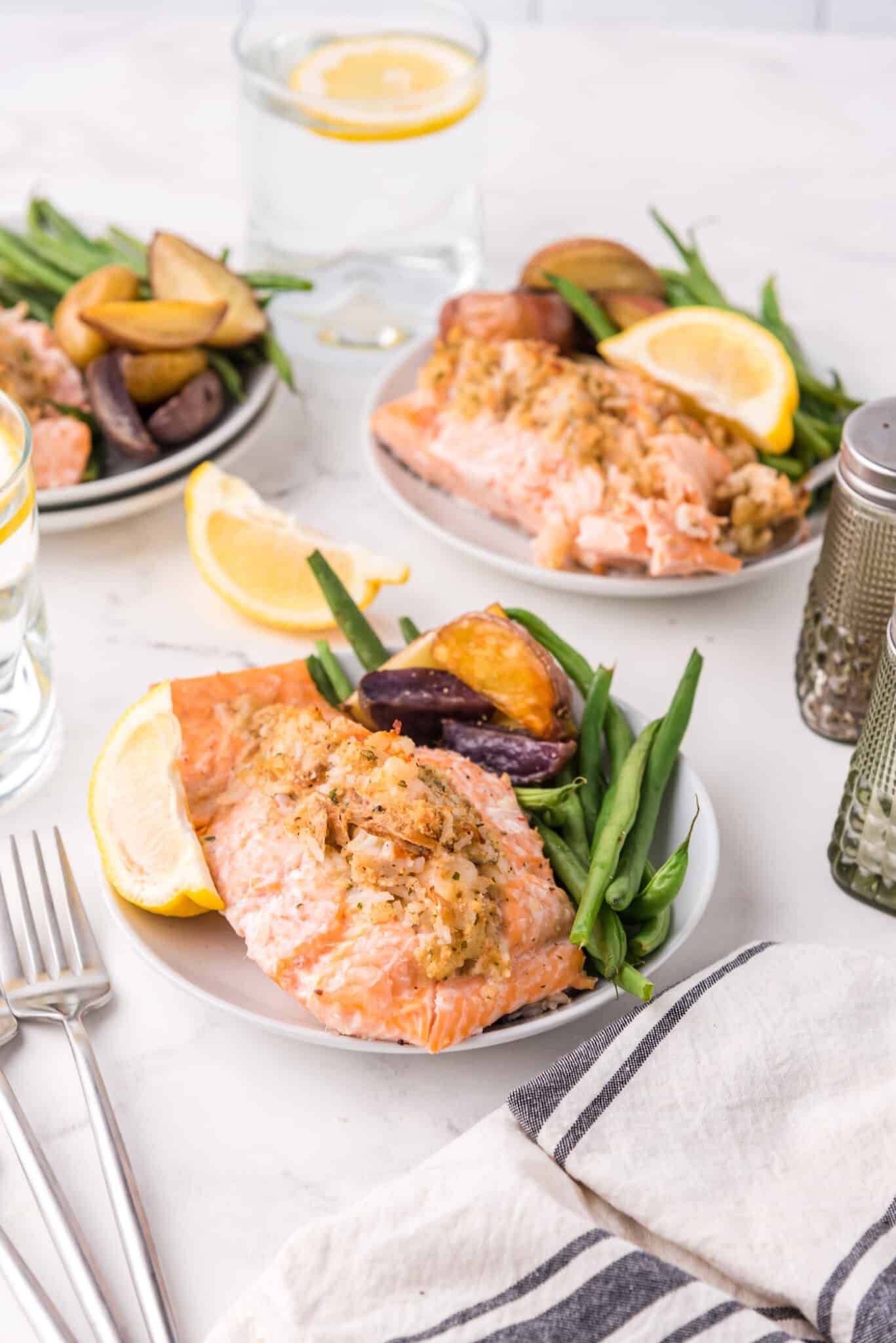 Stuffed salmon with green beans and potatoes on white plates.