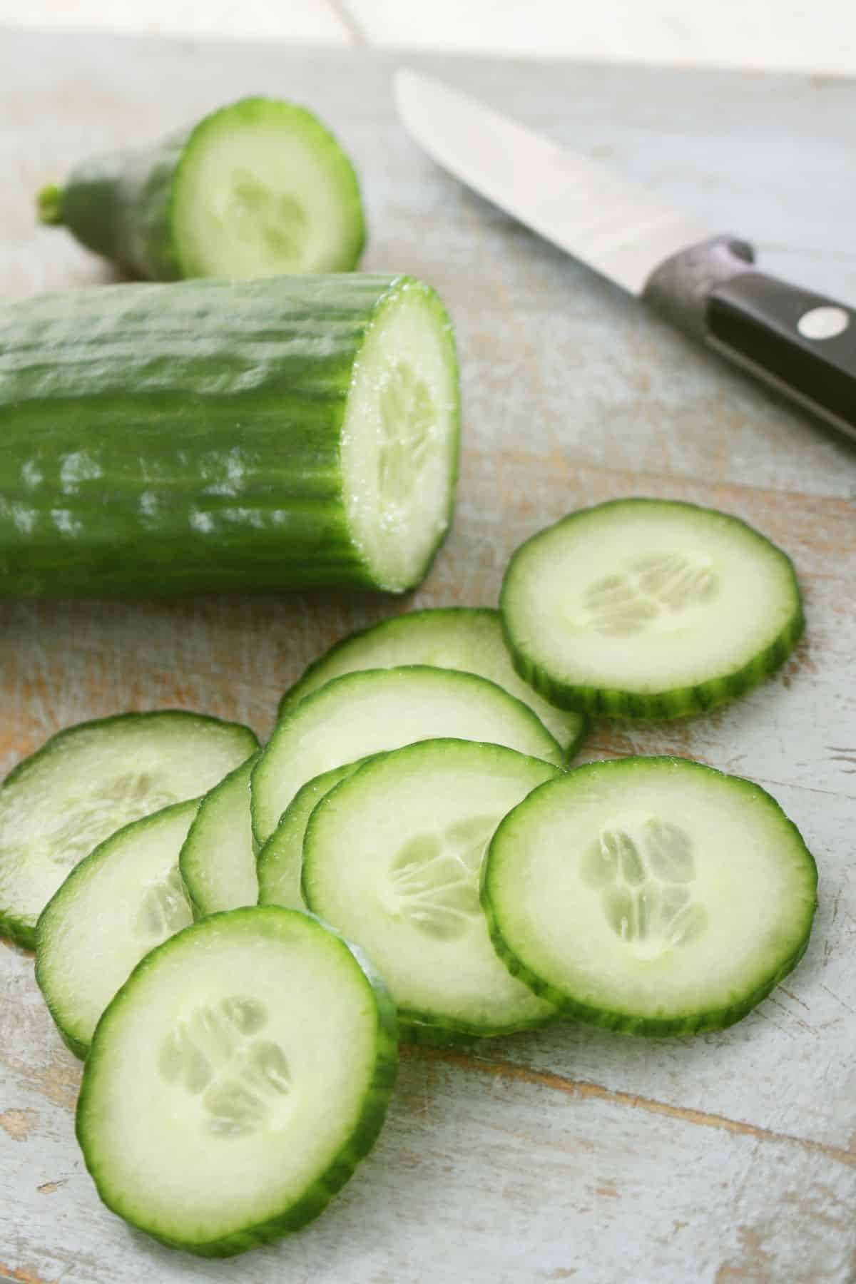 Halved and sliced cucumber on wooden surface.