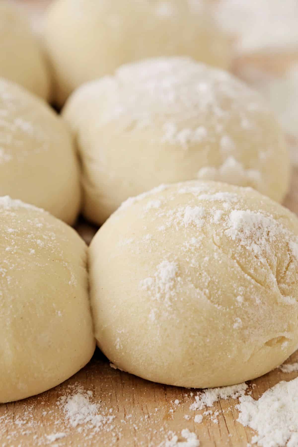 Gluten free dinner rolls shaped and resting on a wooden board.