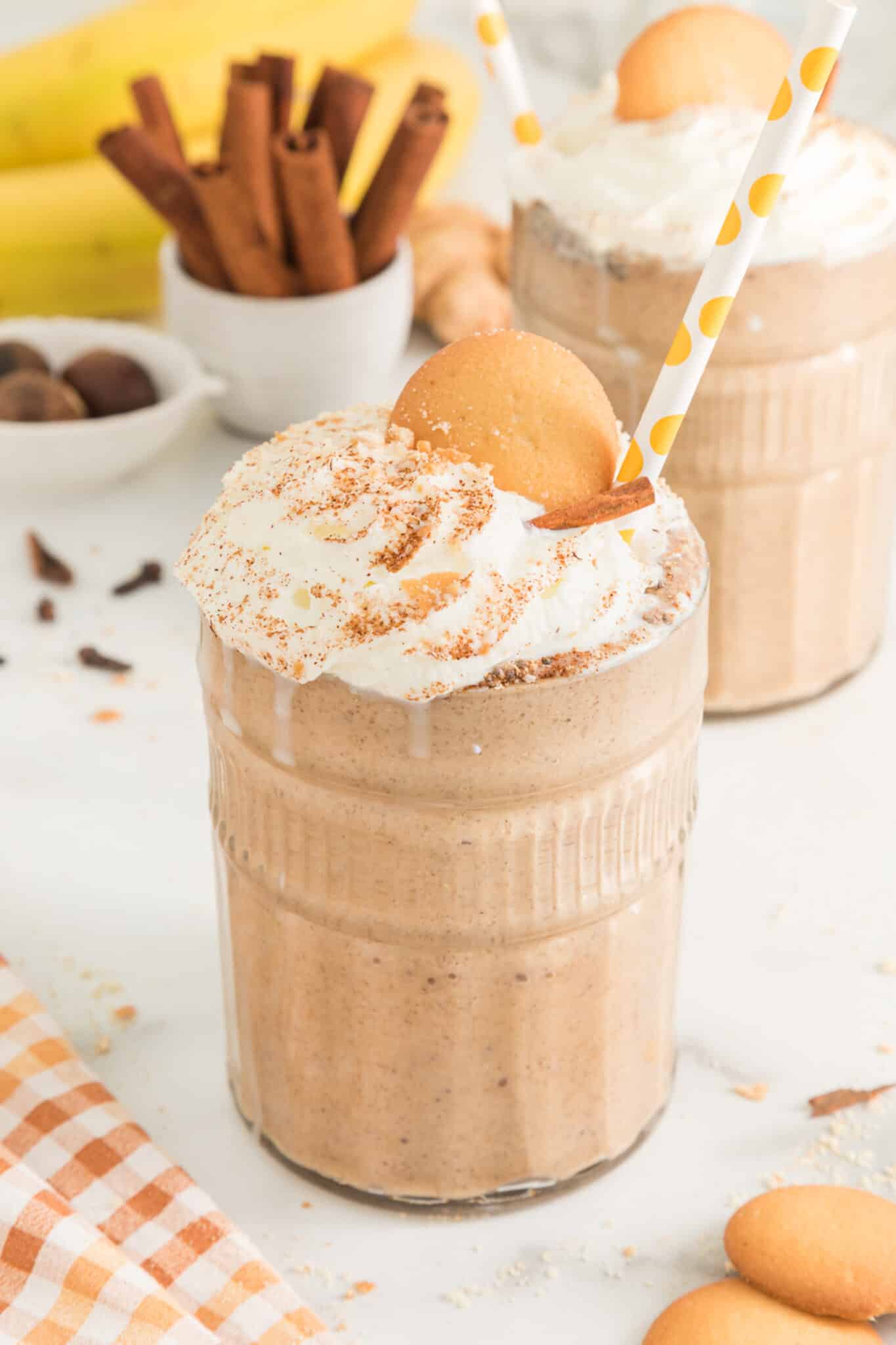 Two glasses of gingerbread smoothie topped with whipped cream and cookies.