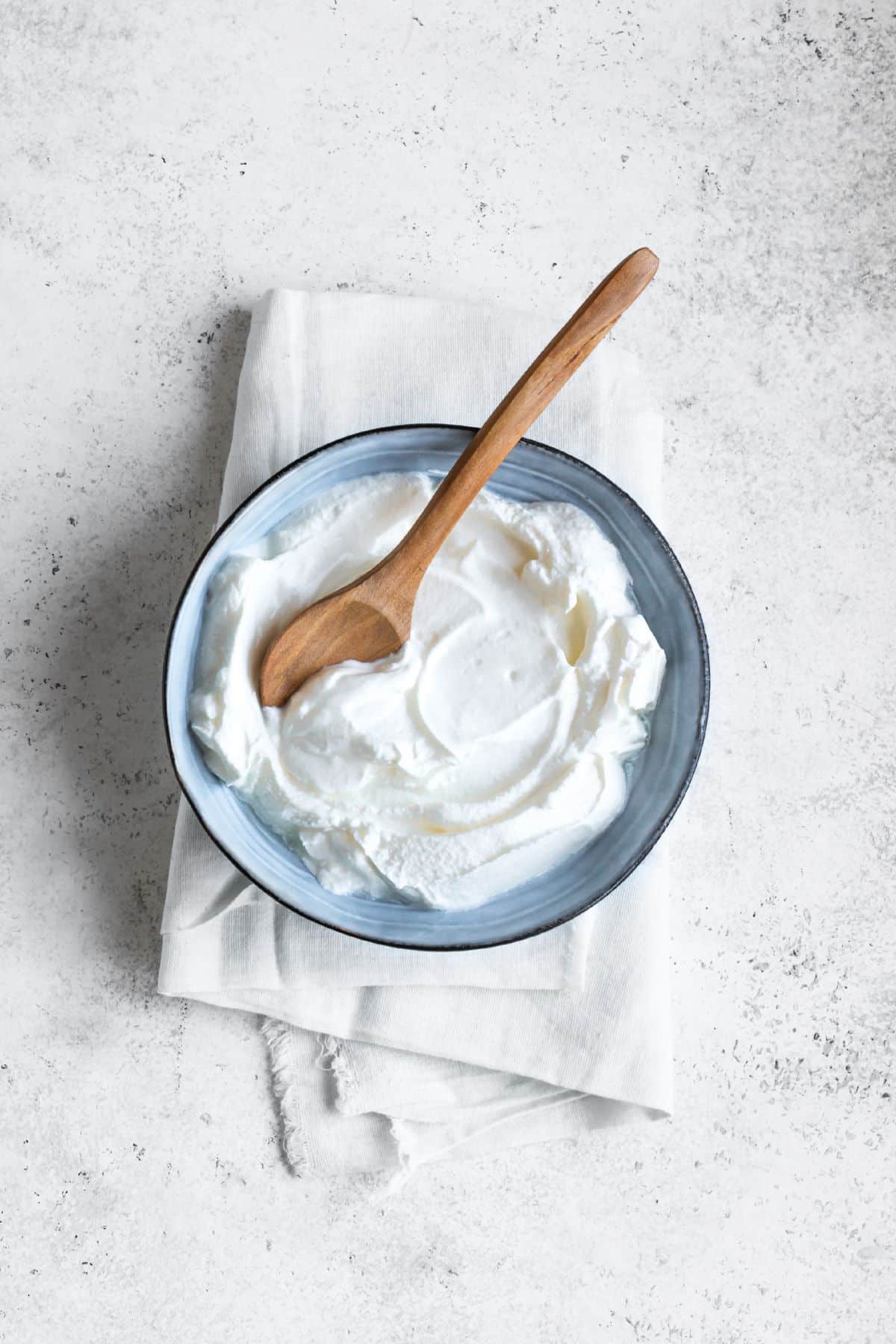 Bowl of greek yogurt with spoon on light surface.