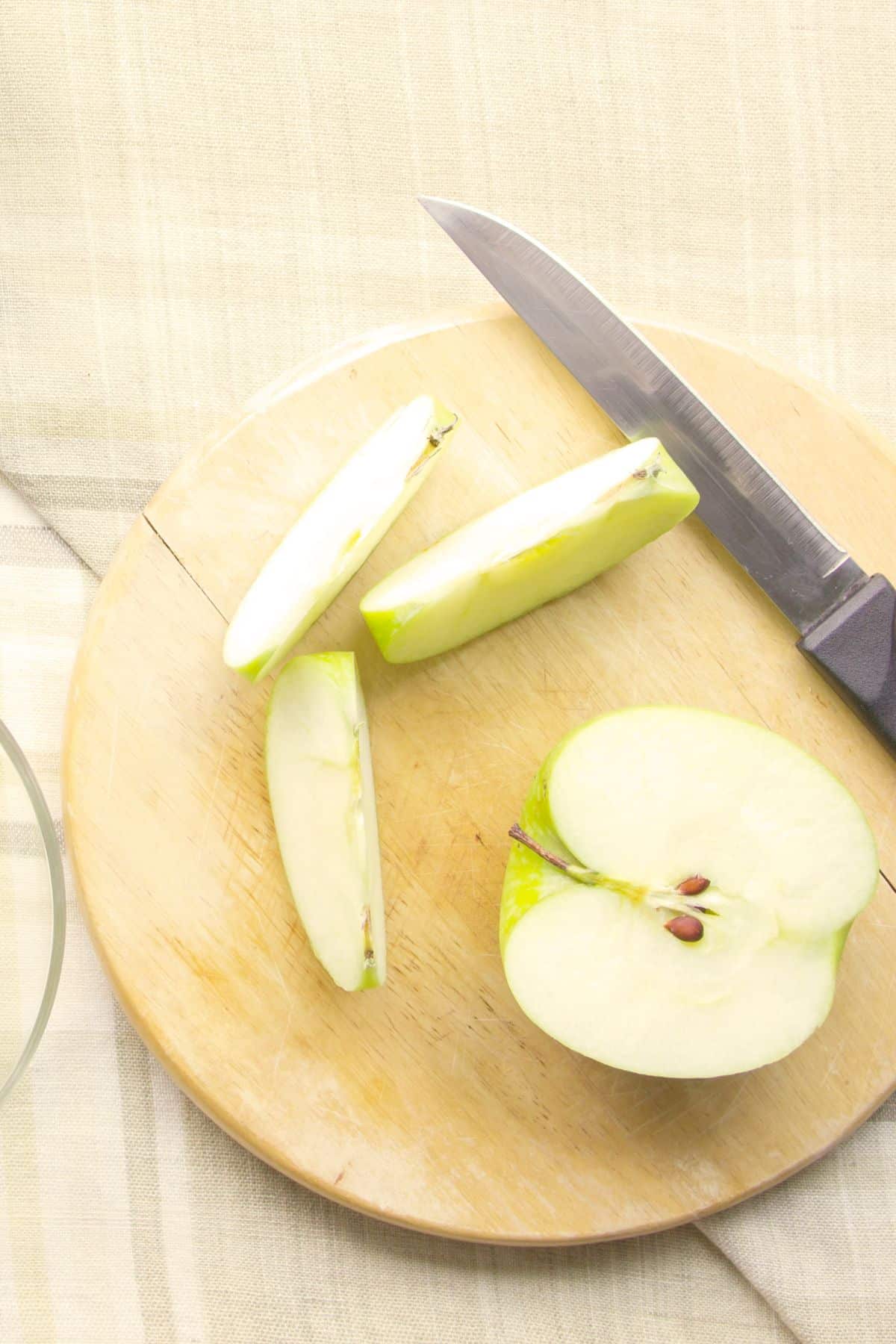 Halved and sliced green apple on wooden cutting board.