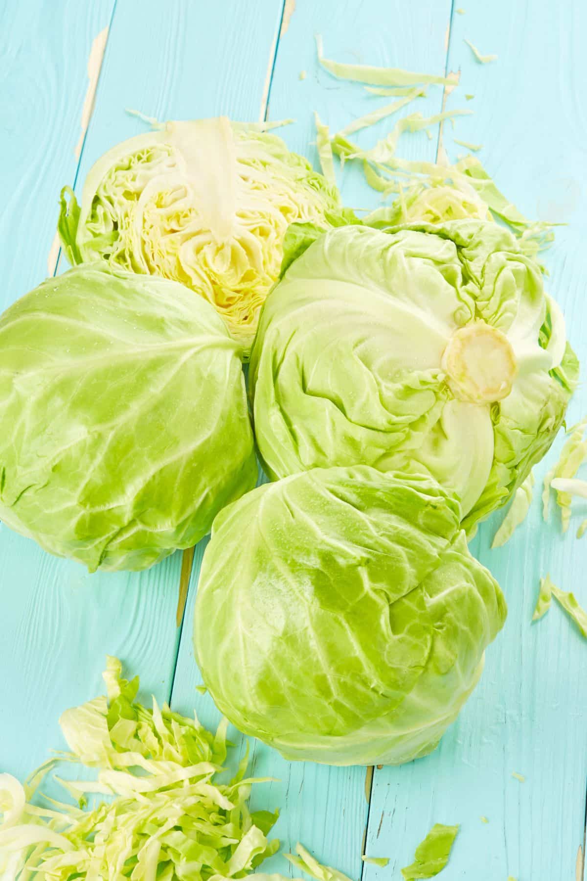 Halved and whole green cabbage on painted wooden surface.