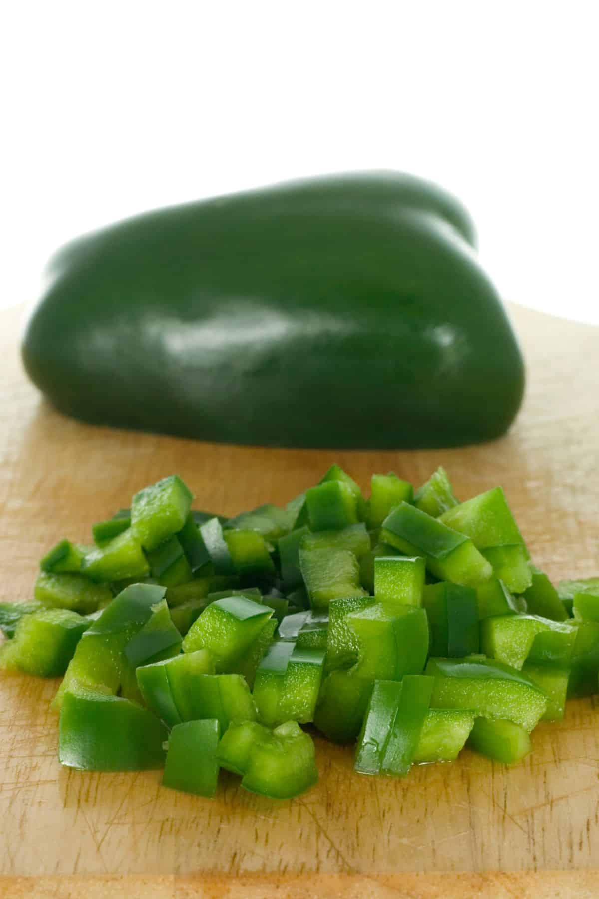 Halved and chopped green pepper on wooden cutting board.