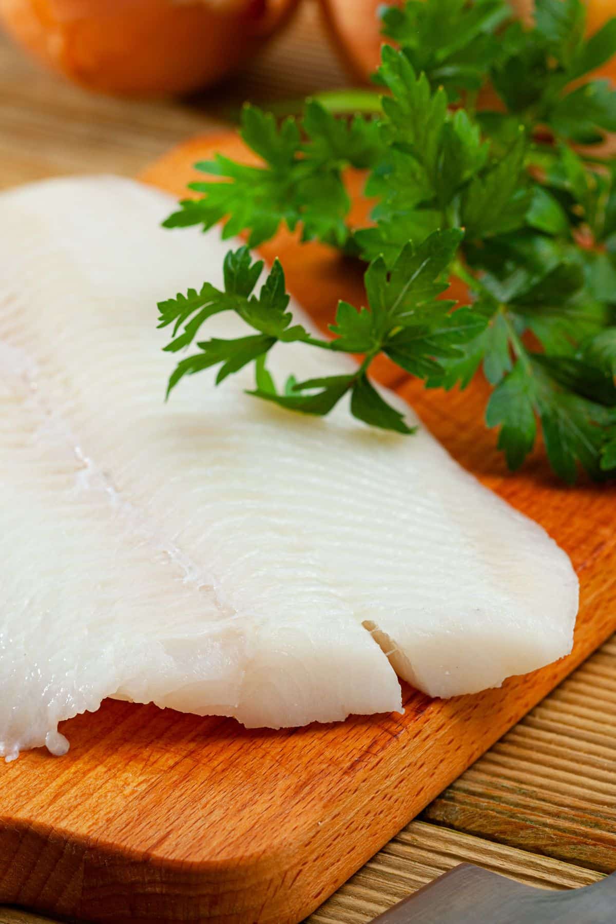 Halibut fillet with fresh parsley on wooden cutting board.