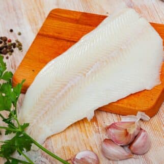 Halibut fillet with fresh parsley on wooden cutting board.