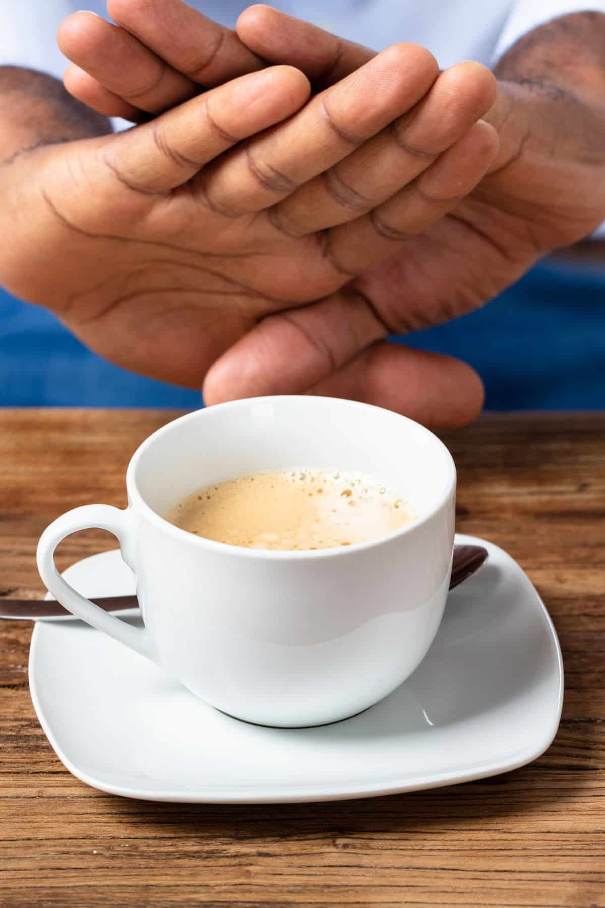 two hands crossed in front of a mug of coffee.