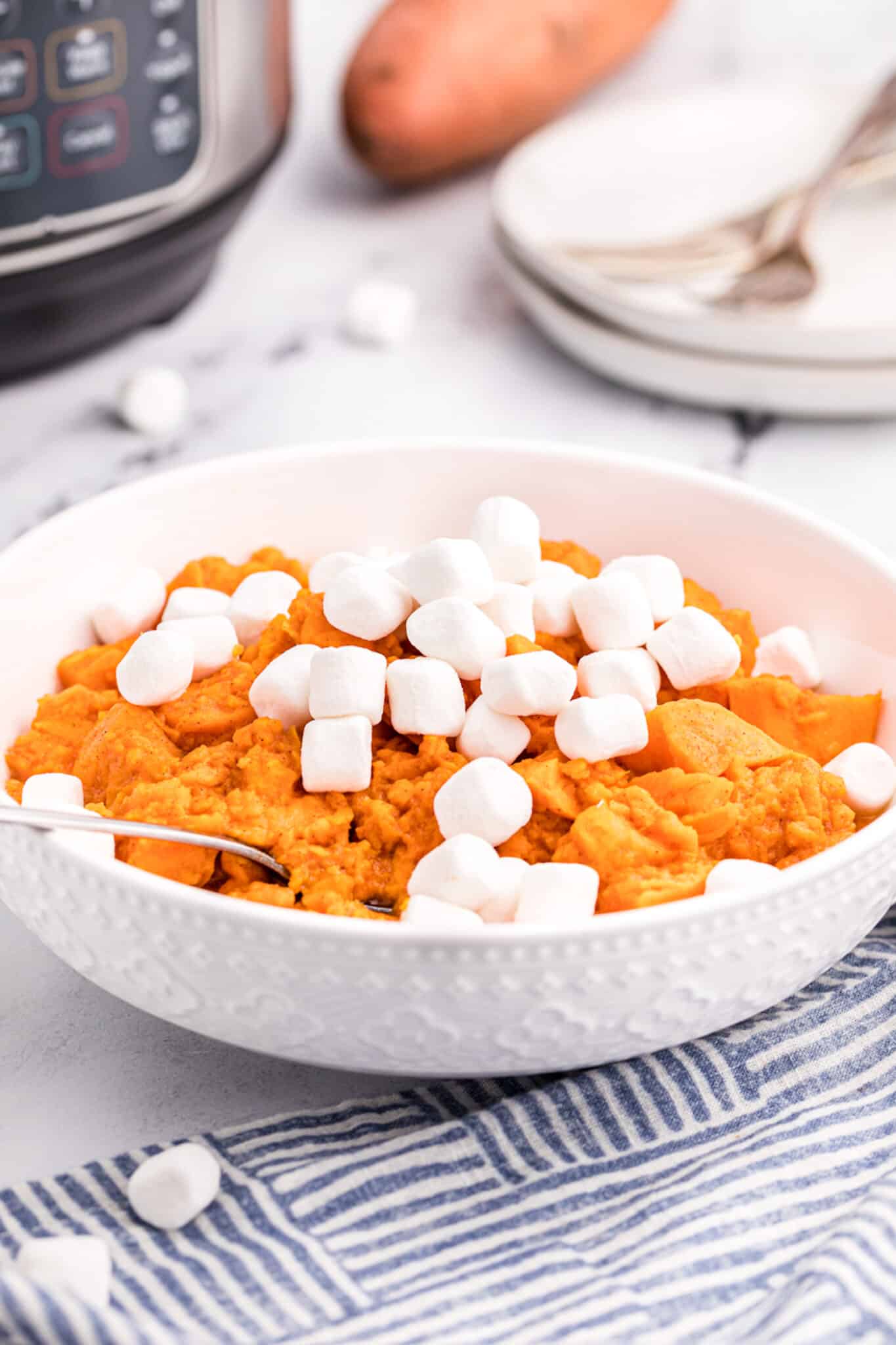 A white serving bowl with candied yams topped with marshmallows.