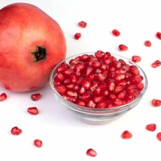 A whole pomegranate next to a small glass bowl of seeds.