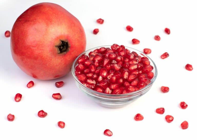 A whole pomegranate next to a small glass bowl of seeds.