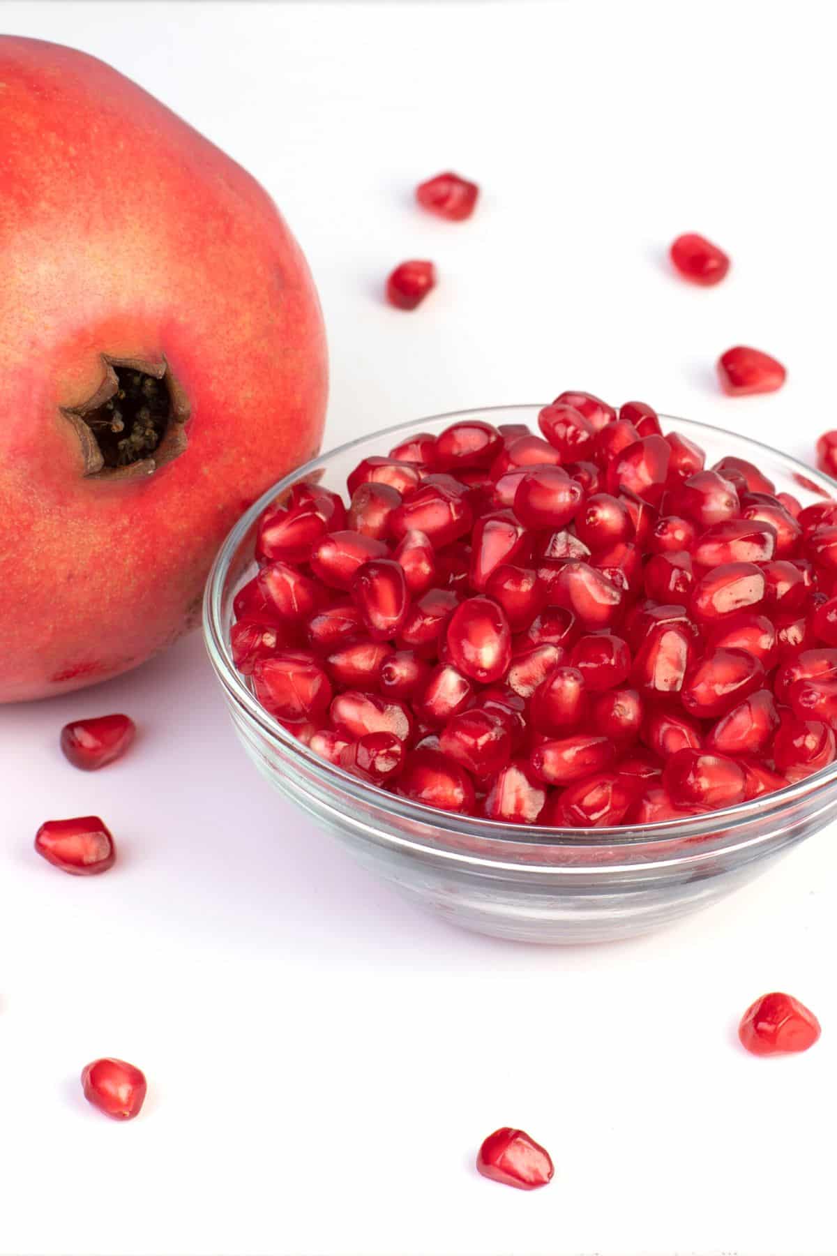 A whole pomegranate next to a small glass bowl of seeds.