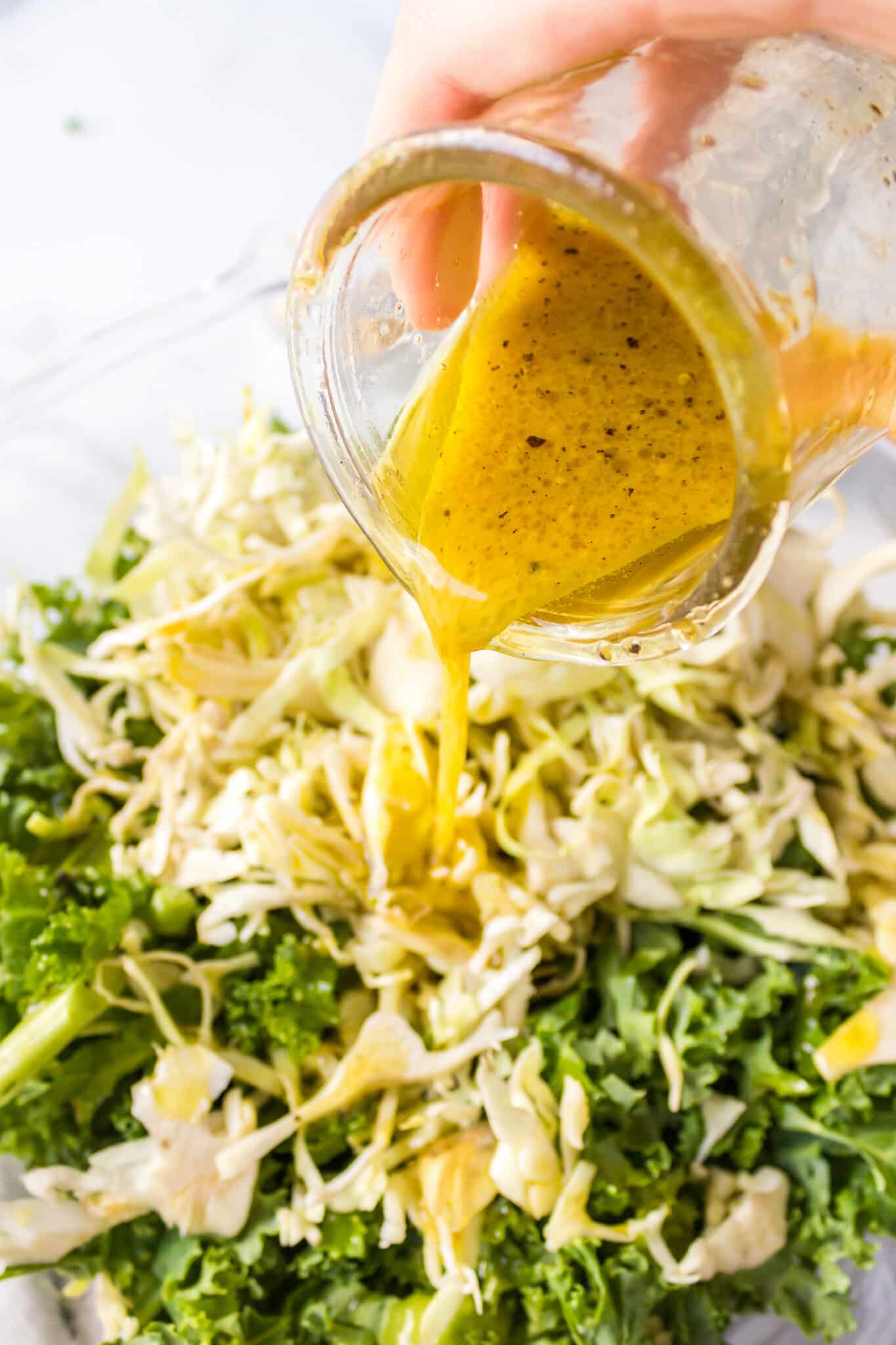 A jar of dressing being poured over a kale salad.