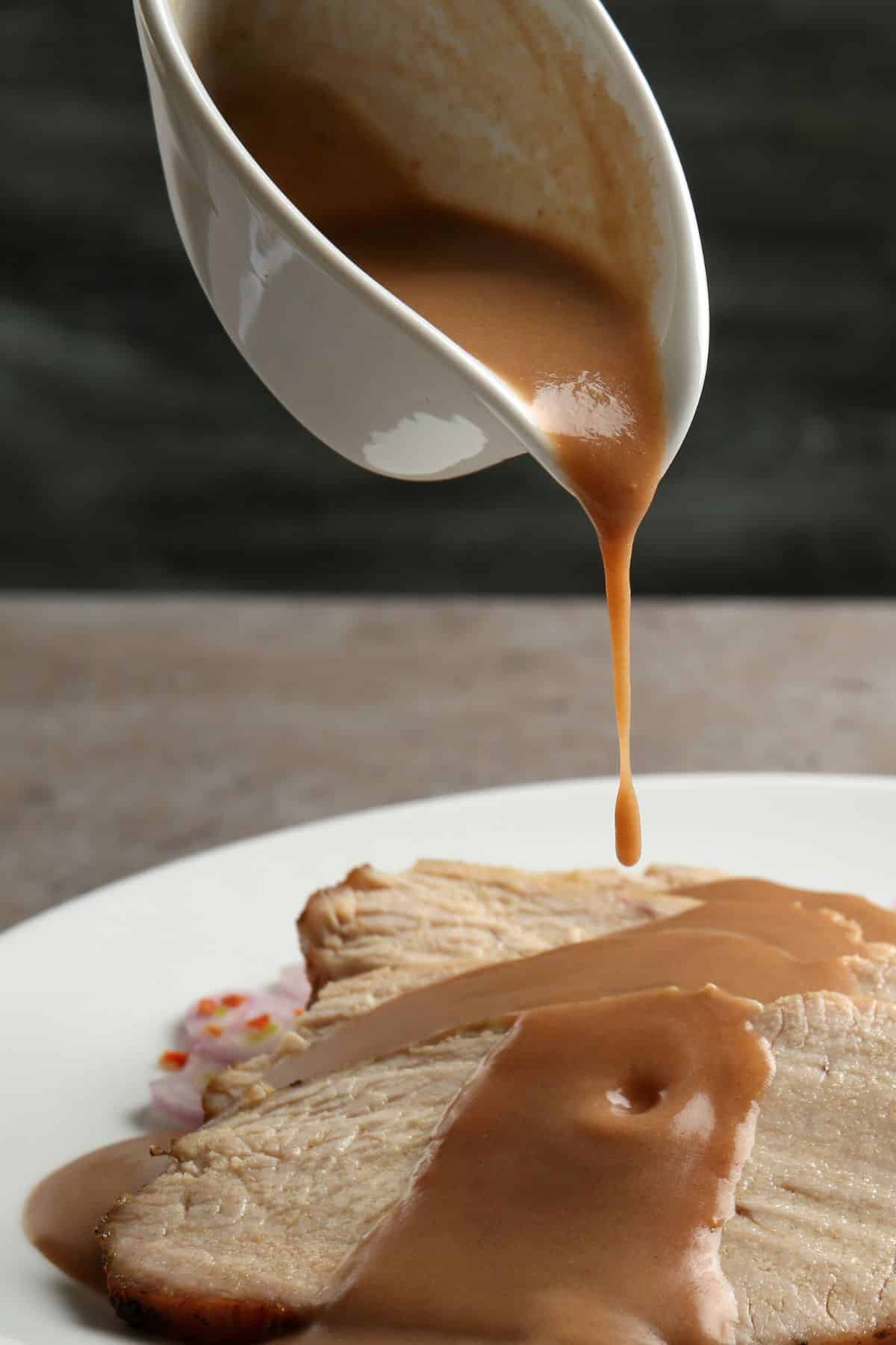A gravy boat pouring gravy over sliced turkey on a plate.