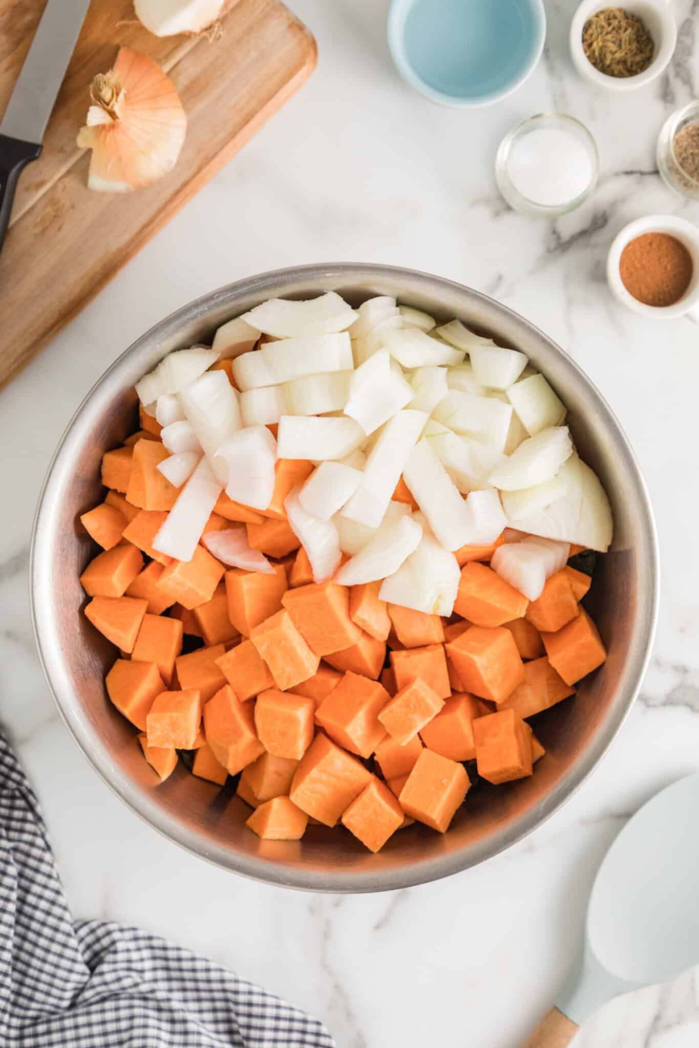 Diced sweet potatoes and white onion in a stainless bowl.