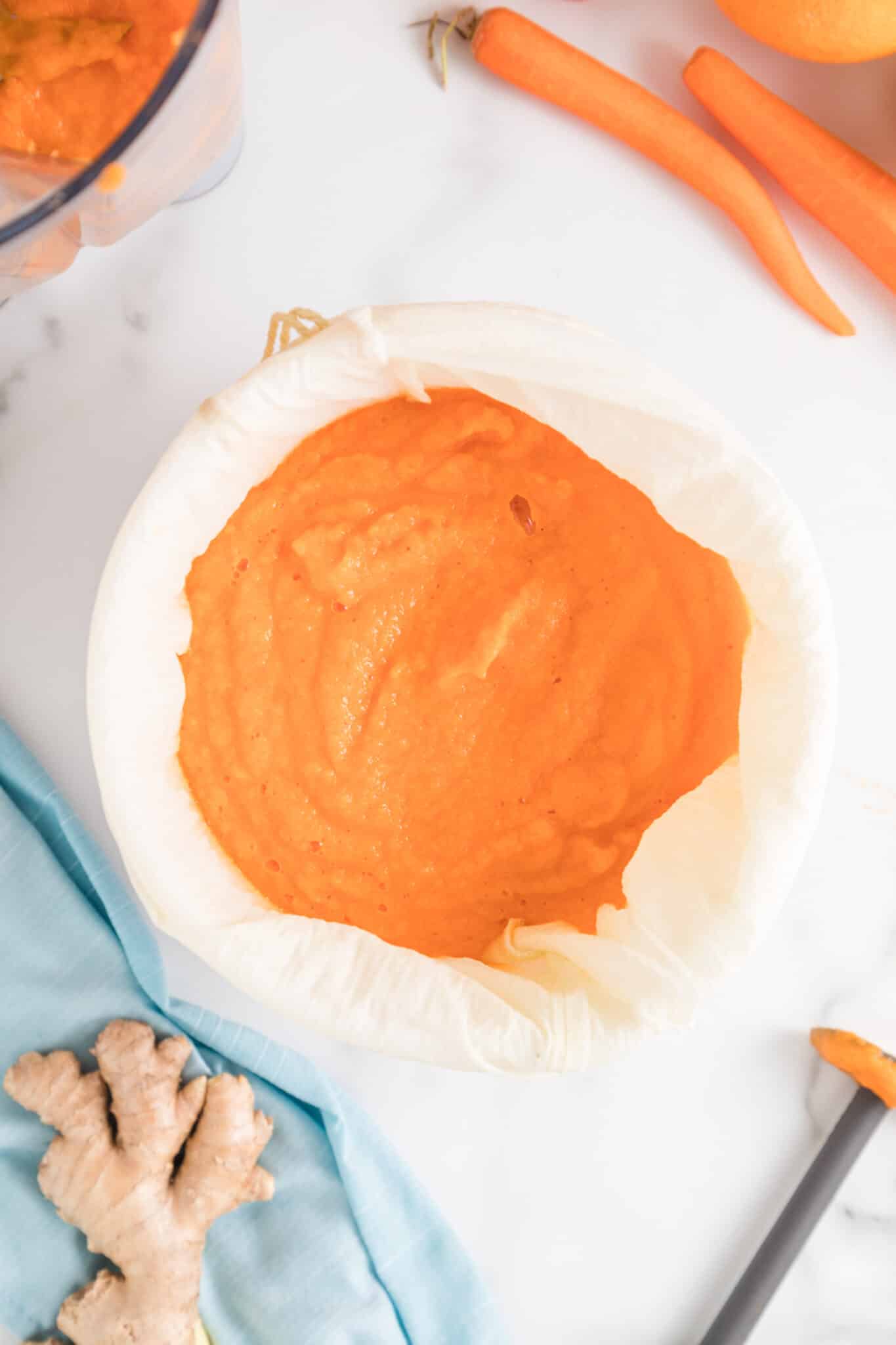 Orange juice in a nut milk bag straining over a bowl.