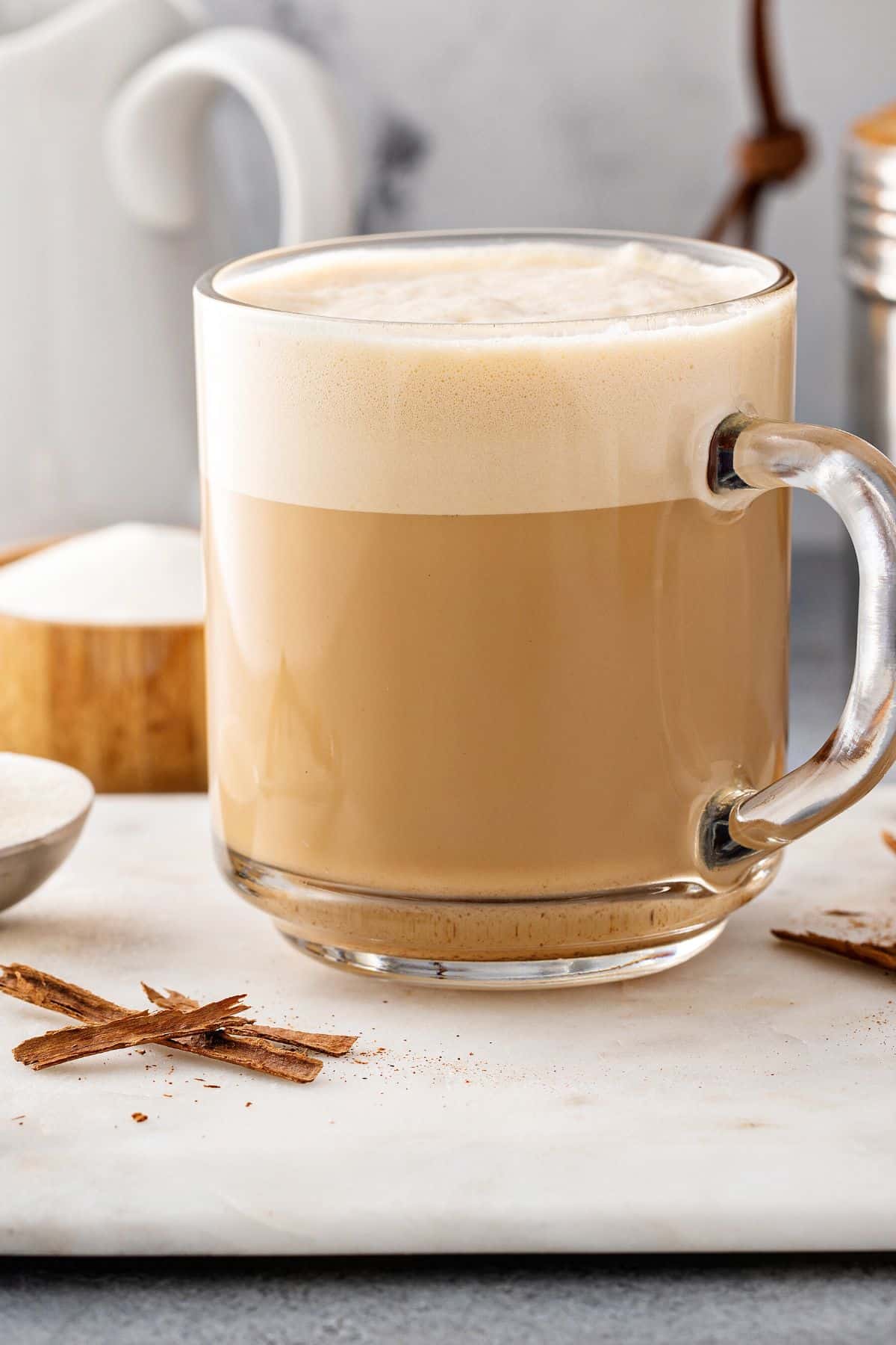 A clear glass mug of protein coffee topped with foam.